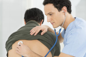 Young Male Doctor Checking Patient With Stethoscope In Hospital